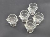 six clear glass cups and saucers sitting on a black surface
