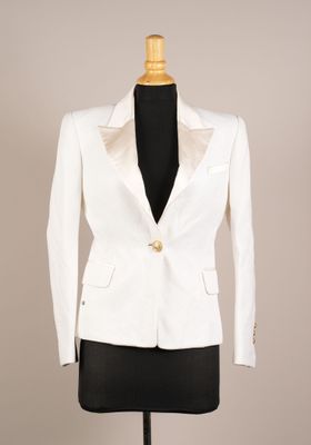 La veste blanche est présentée sur un mannequin posé sur un socle.