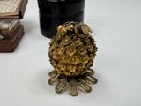 a small gold pine cone sitting on a table next to a potted plant