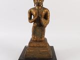 statue en bronze représentant une personne assise sur un socle, les mains jointes