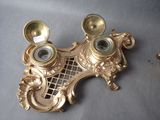 a gold clock on the wall next to a gold candle holder