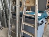 une pile d'échelles dans un garage, avec une poubelle bleue en arrière-plan