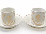 two cups and saucers with gold designs on them