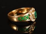 a close up of a gold ring with green stones on a black surface