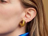 La femme porte un t-shirt bleu et une paire de boucles d'oreilles dorées.