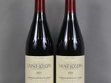 two bottles of wine sit on a glass table in front of a gray wall