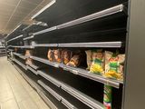 de nombreuses étagères vides dans un supermarché, sur lesquelles se trouvent des produits alimentaires