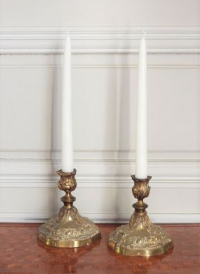 une paire de bougeoirs en laiton posés sur une table en bois devant un mur blanc
