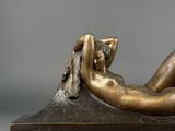 bronze sculpture of a woman laying on a rock with her legs crossed