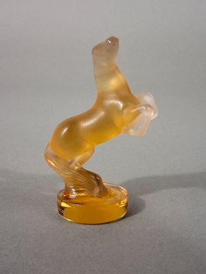 un cheval en verre posé sur un socle jaune, lui-même posé sur une surface grise