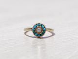 une image représentant une bague en or ornée d'une pierre turquoise et d'une pierre blanche au centre