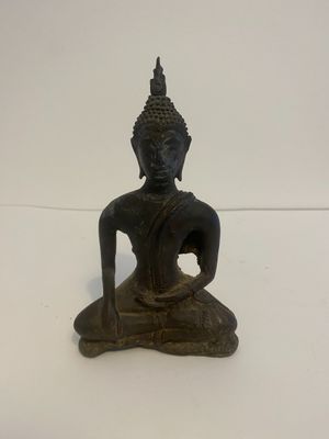 une vieille statue en bronze représentant un Bouddha assis sur un socle blanc