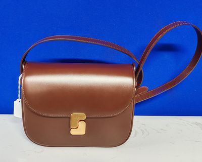 un sac à main en cuir marron orné d'une boucle dorée sur fond bleu