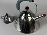 a silver tea kettle with a blue handle next to a silver tea kettle