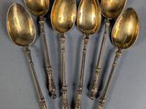 six antique spoons are lined up in a row on a gray surface