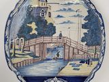 assiette bleue et blanche ornée d'une peinture représentant un pont enjambant une rivière