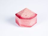 une image représentant une petite boîte rose avec un couvercle, posée sur une surface blanche