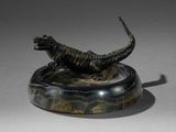 statue d'un lézard posée sur un socle en marbre, sur une surface grise