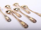 six gold spoons with floral designs on them sitting on a white surface