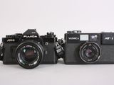 two cameras sitting next to each other on a white surface