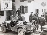 a group of men standing in front of an old jeep