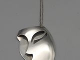un masque en argent suspendu à une chaîne sur un mur blanc