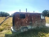 un vieux bus rouillé, garé dans un champ, avec des arbres en arrière-plan