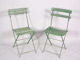 pair of green metal folding chairs against a white background