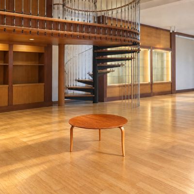 une table en bois au milieu d'une pièce, avec un escalier en colimaçon en arrière-plan