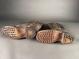 a pair of brown leather boots with studded soles on a gray surface