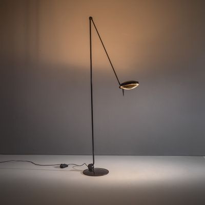 un lampadaire noir posé sur une surface blanche, dont la lampe est allumée