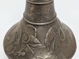 a silver vase with birds on it on a white surface