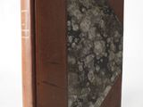 an old book with a brown cover sitting on top of a white table