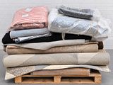 pile of folded blankets on pallets in front of a white brick wall