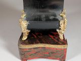 an image of a black and gold clock sitting on top of a wooden stand