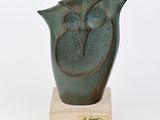 un vase vert orné d'un oiseau, posé sur un socle en bois