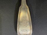 a silver spoon with a design on it sitting on a black surface