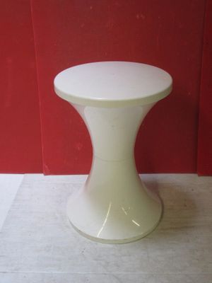 un petit tabouret blanc posé par terre devant un mur rouge