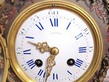 a gold clock with blue roman numerals on it