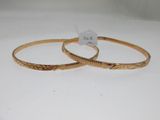 two gold bang bracelets with engraved designs on them on a white surface