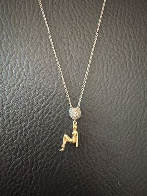 a gold necklace with a small figure sitting on a black leather surface