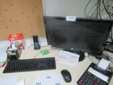 a desk with a computer, keyboard, calculator, and other items on it