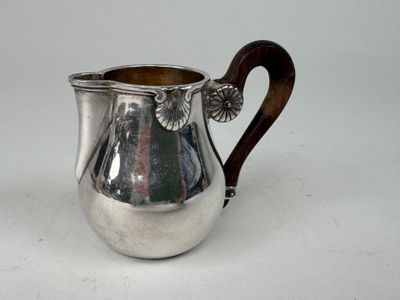 une cruche ancienne en argent avec une poignée en bois, posée sur une surface blanche