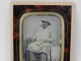 une vieille photo d'une femme assise sur une chaise, coiffée d'un chapeau