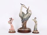 trois figurines d'oiseaux posées sur un socle en bois, avec une femme en robe rose