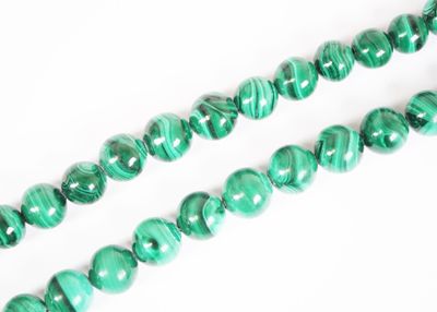 un gros plan sur un collier de perles de marbre vert posé sur une surface blanche