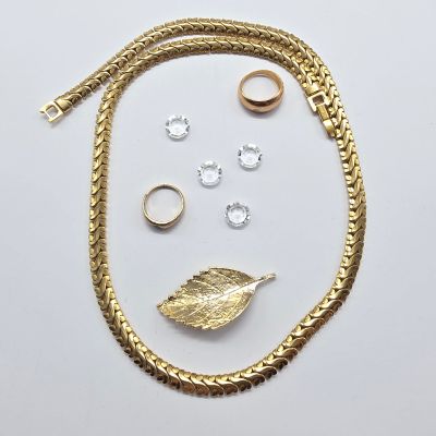 un gros plan sur un collier en or, une bague et d'autres bijoux posés sur une surface blanche