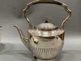 a silver tea pot and a silver cup on a table