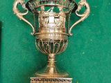 un trophée en argent posé sur une surface verte, à côté d'une horloge
