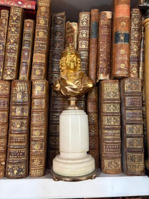 many old books on a shelf with a statue on top